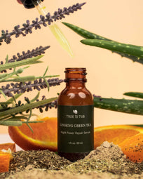 Bottle of Anti Aging Serum with dropper held by a hand, surrounded by lavender, aloe vera, & orange slices