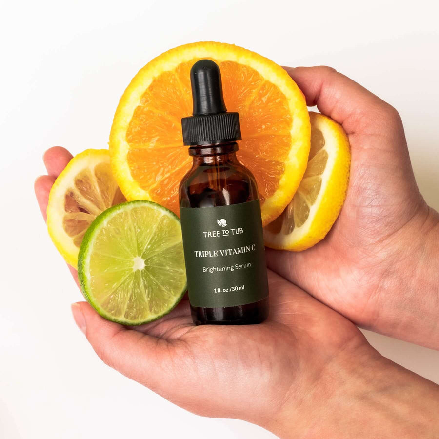 Two open hands holding the Triple Vitamin C serum and slices of orange, lemon and lime