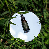 Double Hyaluronic Serum resting on top of a mirror placed on a patch of real grass