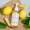  Moisture Boost Biotin and Vegan Collagen Shampoo with Argan Oil, in Sicilian Lemon and Tea Tree Oil scent pump bottle laid on top of a brown sack mat, with lemon leaves and lemon slice garnishes around it 
