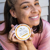 Closeup of a woman smiling and holding the Moisture Defense Shea Body Butter.