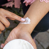 Closeup of opened Moisture Defense Shea Body Butter held by a woman applying the body butter on her wrist.