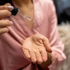 Woman in a pink robe using the serum dropper and putting serum on her palm